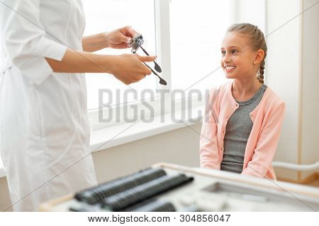 Smiling Pretty Girl With Blue Eyes Patiently Sitting In Medical Cabinet