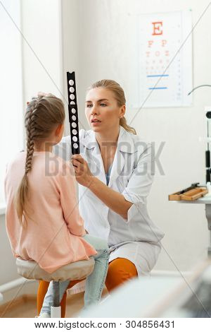 Exploring Eyesight. Blonde Caring Doctor Working With Little Girl While Observing Her Eyes Through M