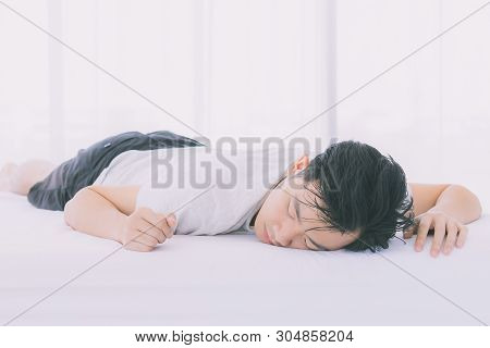 Asian Man Lie Prone On Bed, He In Pajamas In Bedroom.