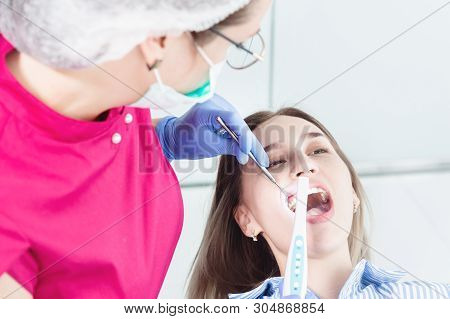 Close-up A Professional Dentist Woman In Glasses And Overalls Examines The Oral Cavity Of A Young Gi