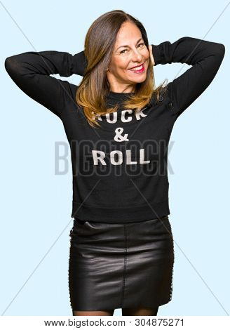 Beautiful middle age woman wearing rock and roll sweater Relaxing and stretching with arms and hands behind head and neck, smiling happy