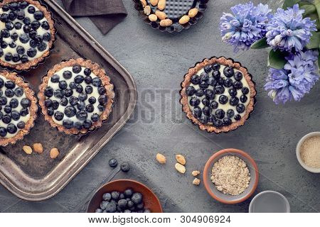 Top View On Wholegrain Blueberry Tarts With Vanilla Cream And Hyacinth Flowers On Dark Background