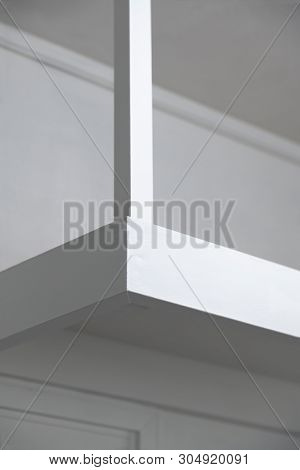 Features of a white room. A pillar and sides of a white wooden shelf in light and shadow.