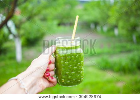 woman's hand holding a jar with green cold-pressed juice, nature background. Healthy eating, detoxing, juicing, body cleancing concept 