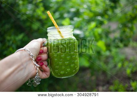 woman's hand holding a jar with green cold-pressed juice, nature background. Healthy eating, detoxing, juicing, body cleancing concept 