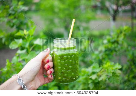 woman's hand holding a jar with green cold-pressed juice, nature background. Healthy eating, detoxing, juicing, body cleancing concept 