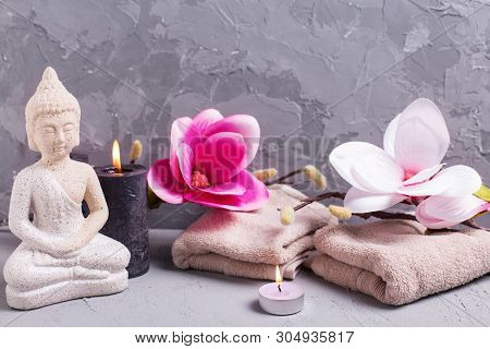 Black Burning Candles , Towels,  Decorative Buddha And Pink Magnolia Flowers On Grey Textured Backgr