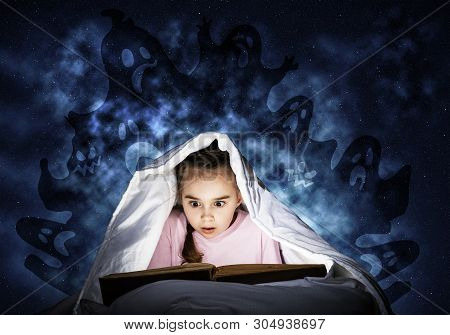 Engrossed Little Girl Reading Book In Bed After Bedtime. Kid In Pajamas With Flashlight Hiding Under