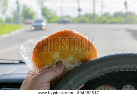 Pie, Belyash With Meat In The Hand Of The Driver In The Car On The Background Of The Steering Wheel 