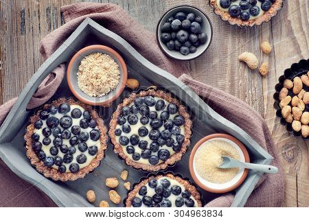 Top View On Wholegrain Blueberry Tarts With Vanilla Cream On Rustic Wooden Background