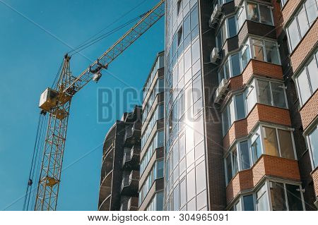 Building Under Construction And Construction Crane Against Blue Sky And Bright Sun On Summer Day. Bo