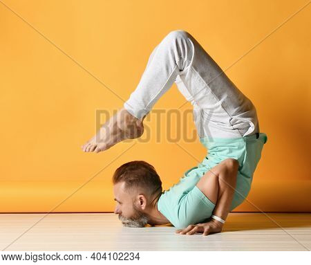Mature Sporty Bearded Grey-haired Man Wearing Sportswear Practicing Yoga In Vrischikasana Scorpion A