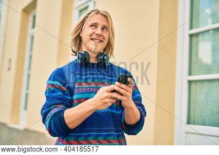 Young scandinavian student man smiling happy using smartphone and headphones at the city.