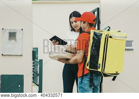 Serious Deliveryman Holding Parcels And Woman Checking Order. Content Courier In Red Cap And Shirt W