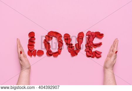 Flat Lay With Love Word From Red Rose Petal Letters, On A Pink Background. Woman Hands Enfold The Wo