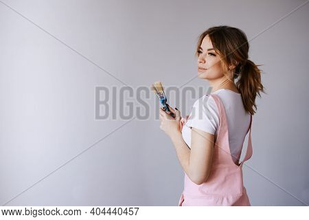 A Woman In A Pink Jumpsuit Is Painting A Wall. Renovation And New Life For Old Things. Brushes And R