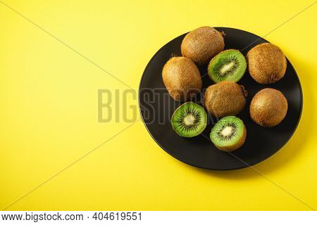 Kiwi Fruits Half Sliced In Black Plate On Vibrant Plain Yellow Background, Copy Space, Angle View