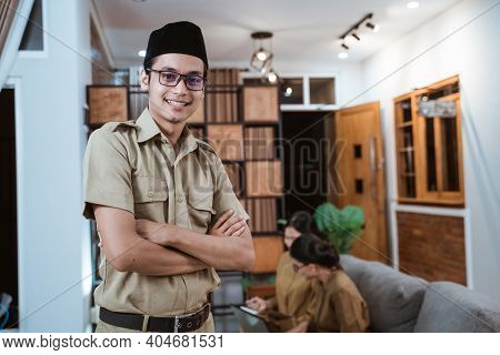 Male Teacher In Civil Servant Uniform Smiling With A Crossed Hand While Working With The Team From H