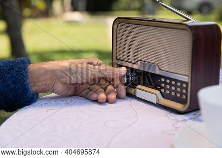 Senior Woman Hand Turning Knob On Vintage Radio In Backyard.