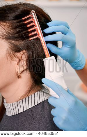 Close Up Of Doctor Trichologist Hand Brushing Female Client Hair With Laser Hair Growth Device. Woma