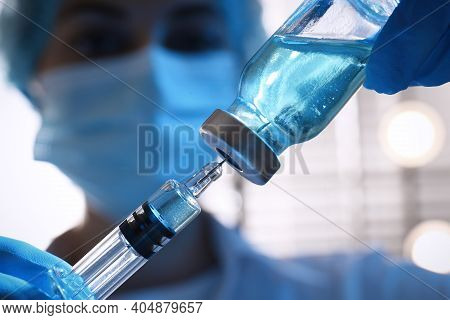 Woman Filling Syringe With Vaccine From Vial On Blurred Background, Closeup