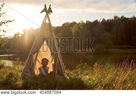 A Little Girl Is Sitting By The Lake. Sunny Akat. Wigwam. Happy Child.
