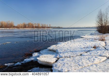 Wide Plain River Partially Covered With Thin Ice, Thick Ice Floes On The Shore Against The Clear Sky