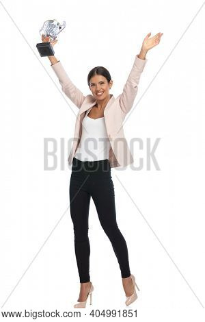 full body picture of smiling young woman in pink jacket holding hands up, holding trophy and smiling on white background in studio
