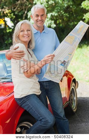 Happy mature couple reading map together by their cabriolet
