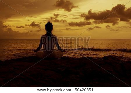 Silhouette of a beautiful Yoga woman in the morning on a beach rock by the sea
