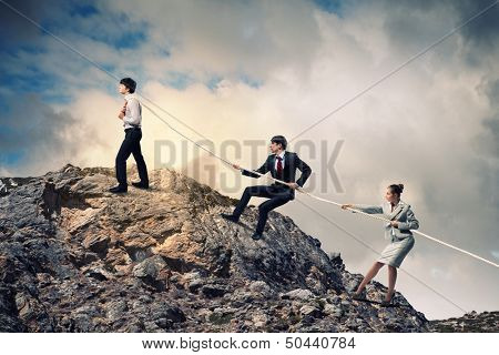 Image of three businesspeople pulling rope atop of mountain