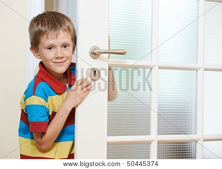 Little smiling boy opening the white door at home