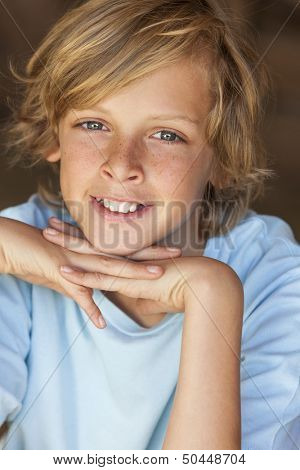 Young happy smiling blond boy child aged about twelve or early teenager resting on his hands