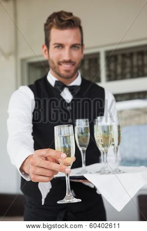 Handsome waiter offering flute of champagne in the patio of restaurant