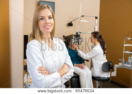 Portrait of confident female eye doctor with colleague examining patient in background