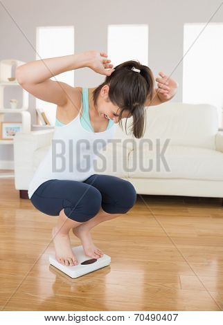 Fit brunette cheering on the weighing scales viargeat home in the living room