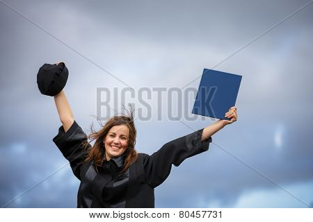 Pretty, young woman celebrating joyfully her graduation - spreading wide her arms, holding her diploma, savouring her success (color toned image; shallow DOF)