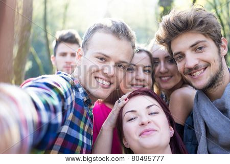 Young people having good time together in park on river and taking selfie