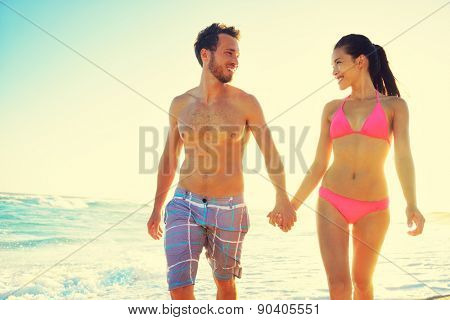 Honeymoon couple romantic in love holding hands at beach sunset. Newlywed happy young couple enjoying ocean sunset during travel holidays vacation getaway. Interracial couple.