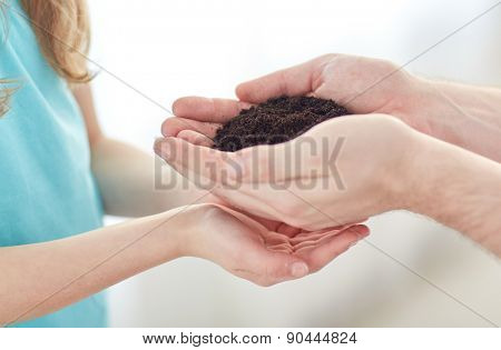 people, charity, family and legacy concept - close up of father and girl holding soil  in cupped hands at home