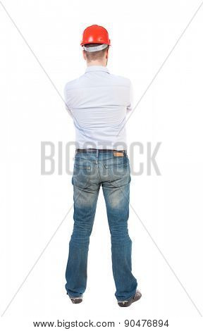 Backview of an engineer in construction helmet stands. Standing young guy. Rear view people collection.  backside view of person. Isolated over white background. Engineer crossed his arms and watches.