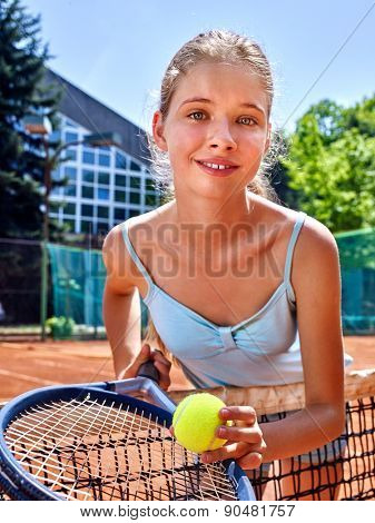 Girl sportsman with racket and ball near net on  tennis court. Green tree ang blue sky on background. Looks over her shoulder. Stadion on background.
