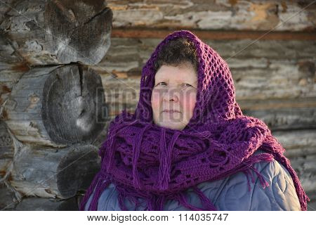 The Russian woman in a shawl warms hands near an izba