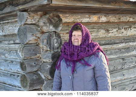The Russian woman in a shawl warms hands near an izba