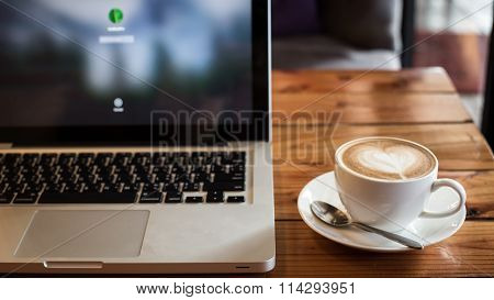 A Cup Of Coffee In A White Cup And Computer Labtop On Mable Table.