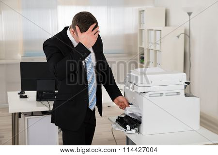 Irritated Businessman Looking At Paper Stuck In Printer