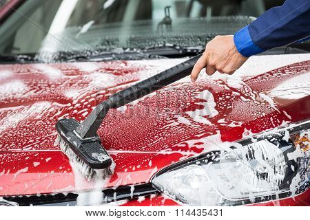 Washer Cleaning Red Car At Service Station