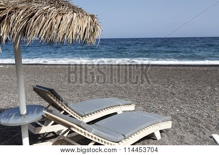 View Of Perissa Beach On The Greek Island Of Santorini With Sunbeds And Umbrellas. Beach Is Covered