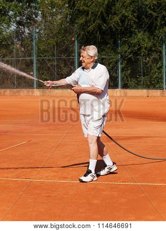 Old men sprinklig tennis court before playing