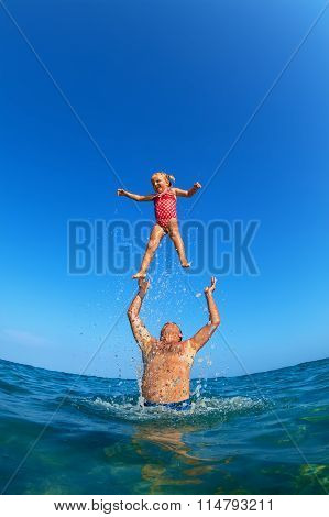 Man Tossing Up Child With Water Splashes In Beach